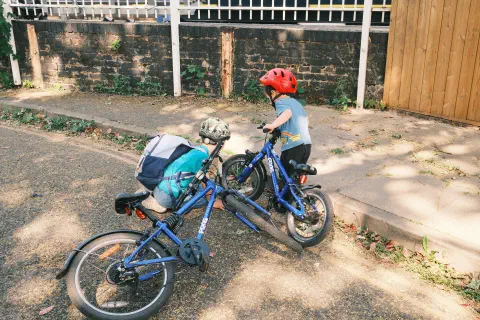 two boys stand by the side of the road, their bikes on the floor as they crouch looking at something by the kerb