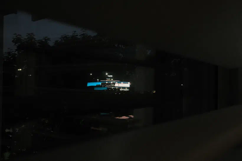 a photo of a night time reflection in an office window, the reflection shows a desk lit up by a computer monitor