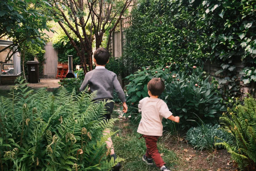 Two boys run out into a garden, the elder of them in school uniform.