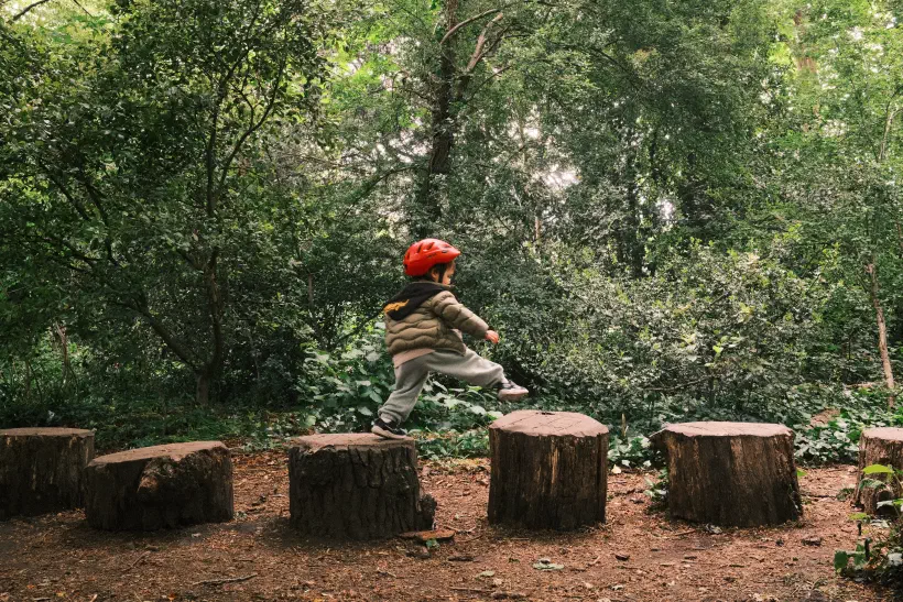 a young boy reaches out to step between two logs