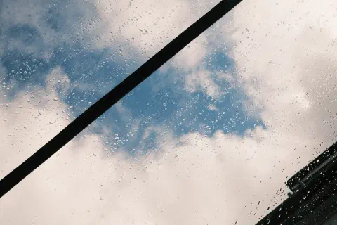 raindrops on a glass window, cloudy blue sky in the background