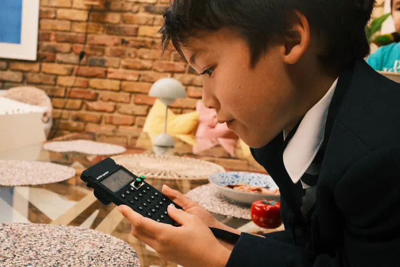 a photo of a boy playing with a Pocket Operator, a plate of food untouched behind him
