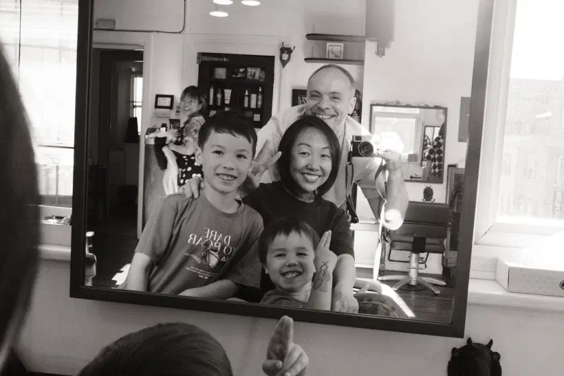 Black and white self-portrait of a family in the mirror at a barbershop.