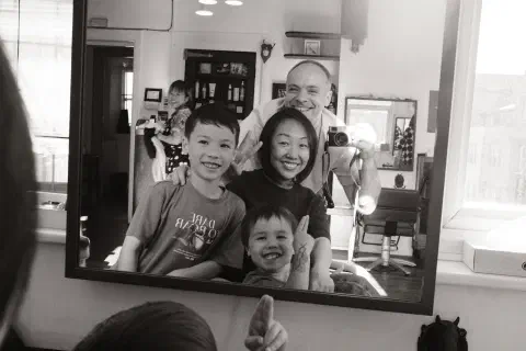 Black and white self-portrait of a family in the mirror at a barbershop.