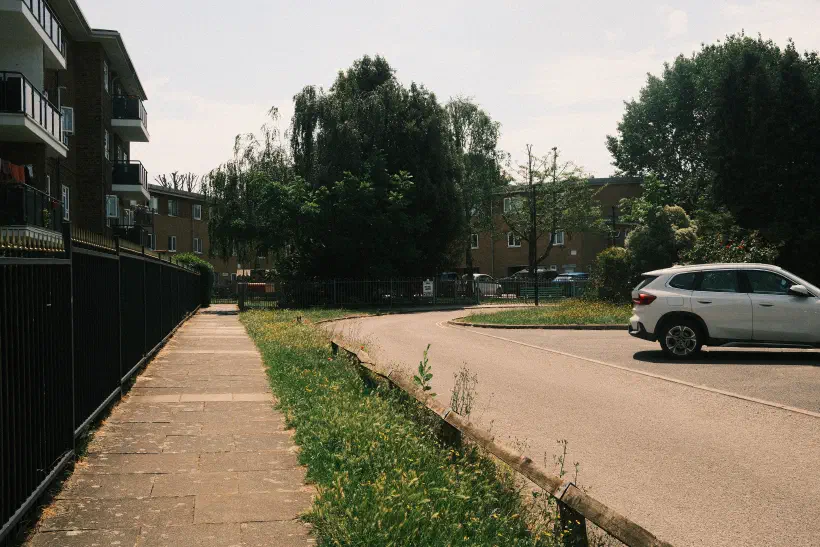 A photo of a deserted street. The pavement and road are lit by the midday sun. No people are out.
